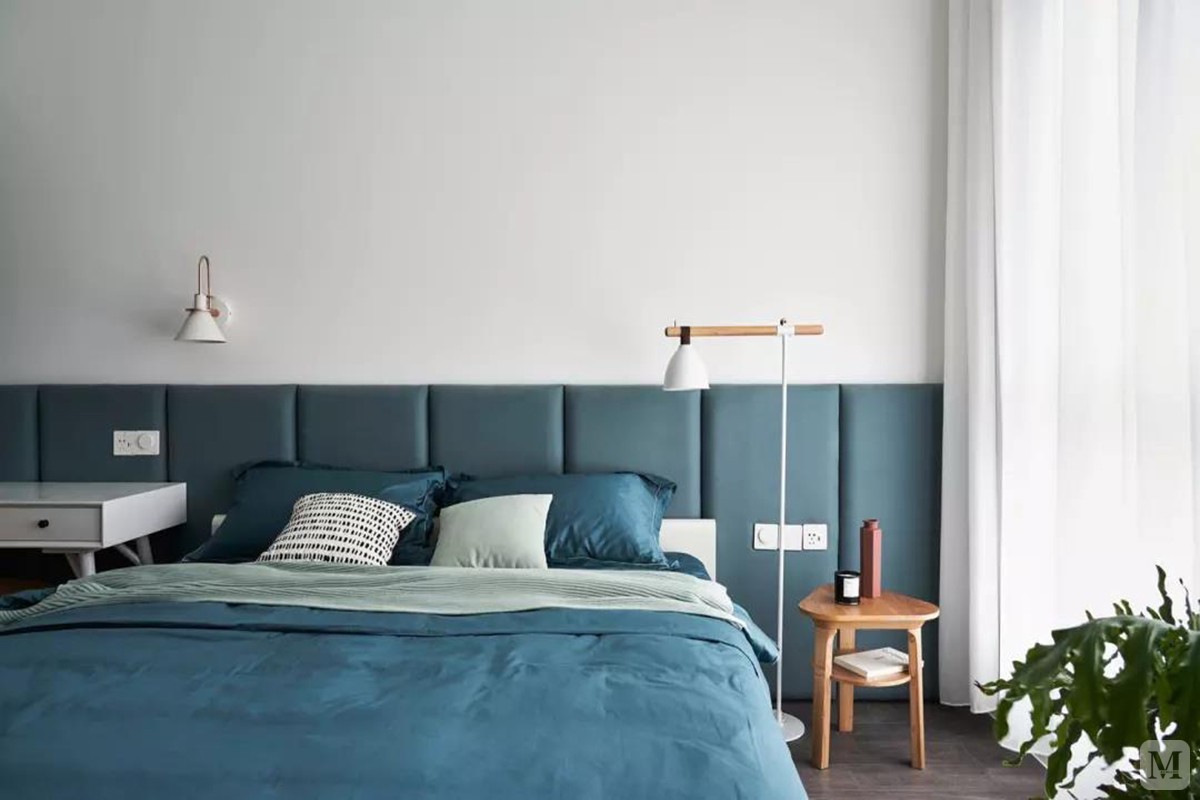 深蓝绿色的软包护墙板同时也是床头靠背，搭配颜色稍浅的床单，配合衣柜处的灰绿色拉帘，透露出森系的自然静谧。